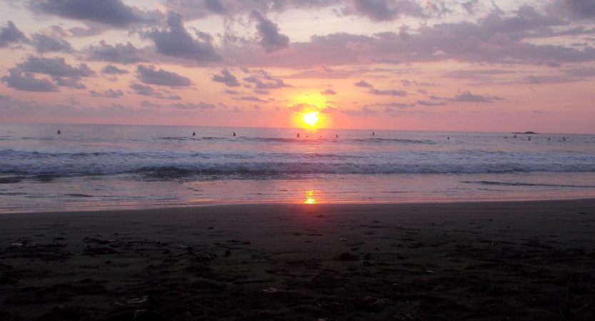The sun sets on the horizon of the ocean. The sky appears in hues of pink and purple.